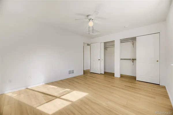 an empty room with wooden floor chandelier fan and windows