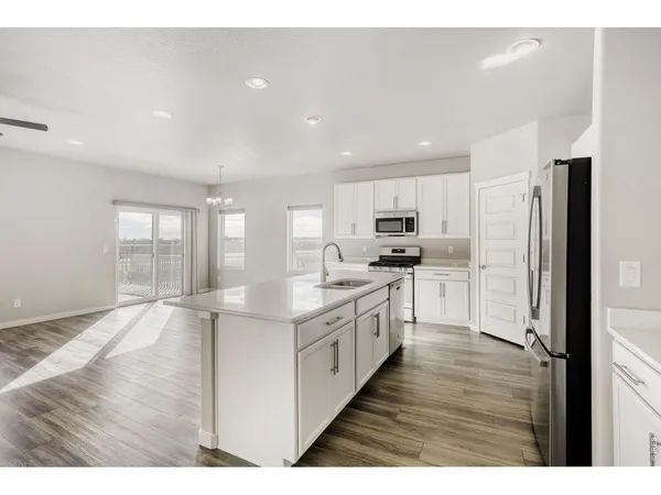 a kitchen with stainless steel appliances granite countertop a refrigerator a sink dishwasher a stove and white countertops with wooden floor