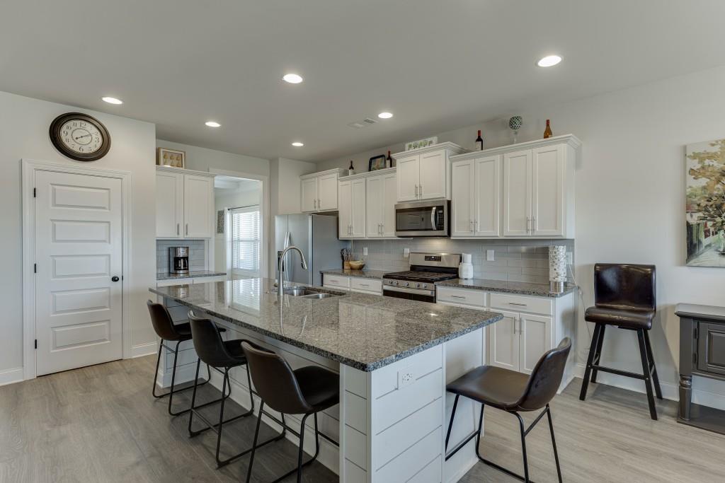 558 Calgary Downs Drive Winder, GA 30680 - Photo 11 of 50 a kitchen with stainless steel appliances granite countertop a stove top oven a refrigerator a sink and a dining table with white cabinets