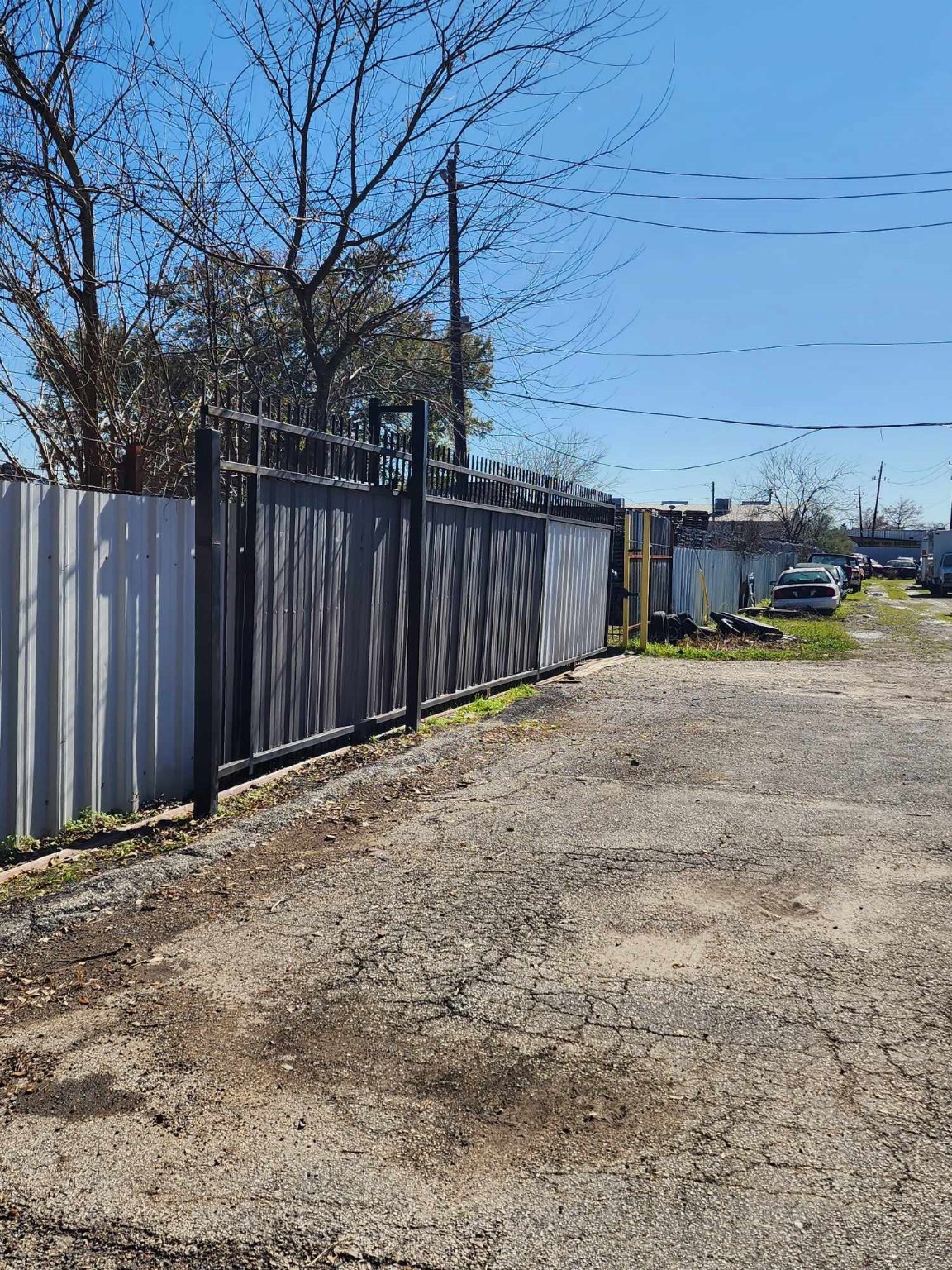 0 Rasmus Drive Houston, TX 77063 - Photo 2 of 11 This photo shows a narrow alleyway with a paved surface and a metal fence on one side. The area appears to be a back access road for properties, with some parked vehicles visible in the distance. The surroundings suggest a quiet, urban environment.