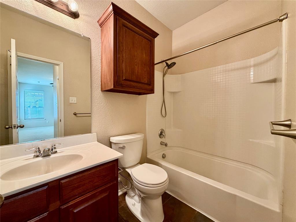 5817 Deck House Road Fort Worth, TX 76179 - Photo 9 of 19 Bathroom featuring a wood-finish vanity with an integrated sink, a white toilet, and a white shower-over-tub combination with a wall-mounted showerhead