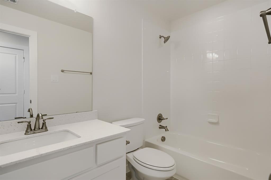828 Stone Grv Road Lavon, TX 75166 - Photo 21 of 27 Bathroom featuring a white vanity with an integrated sink, a speckled light-toned countertop, a frameless wall mirror, and a white bathtub with a tiled surround
