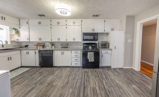 a kitchen with stainless steel appliances granite countertop a stove top oven a sink dishwasher and a refrigerator with wooden floor