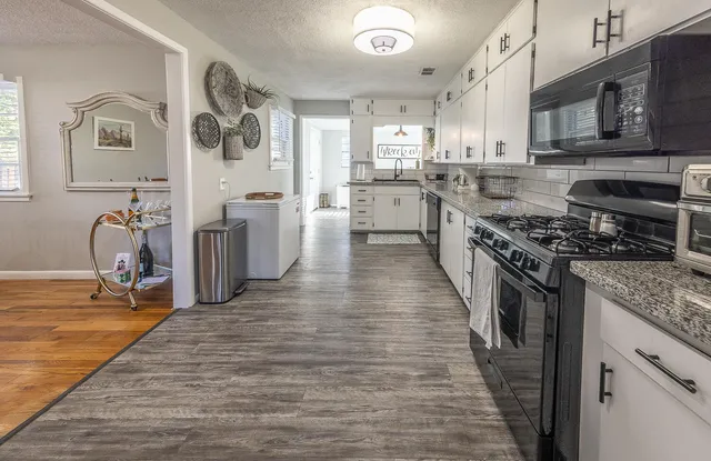 a kitchen with granite countertop a stove top oven a sink dishwasher and a refrigerator with wooden floor