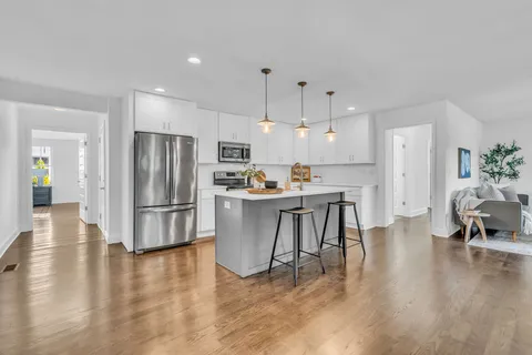 a kitchen with stainless steel appliances kitchen island a refrigerator a stove a dining table and chairs with wooden floor