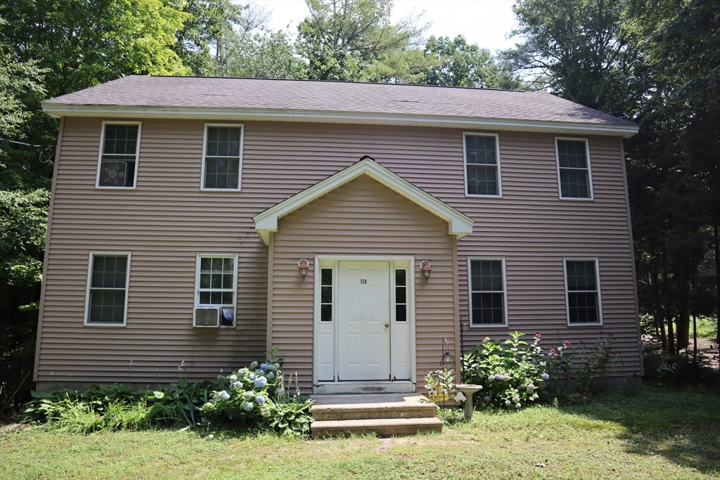 a view of a house with a yard plants and large tree