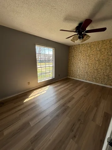an empty room with wooden floor fan and windows