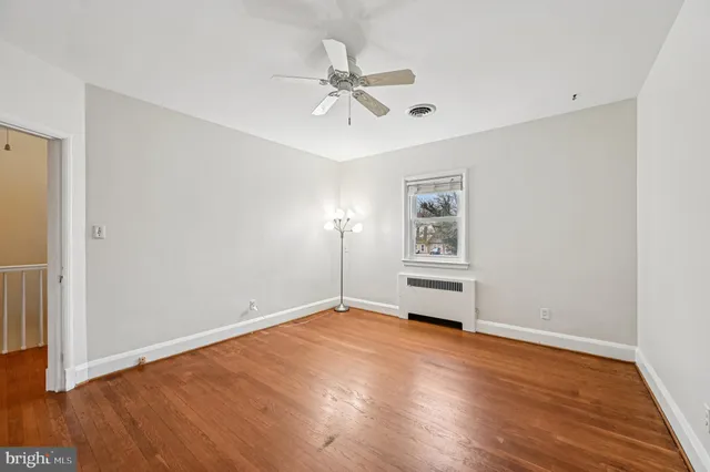 a view of an empty room with wooden floor and a ceiling fan