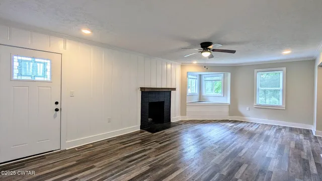 a view of an empty room with wooden floor fireplace and a window