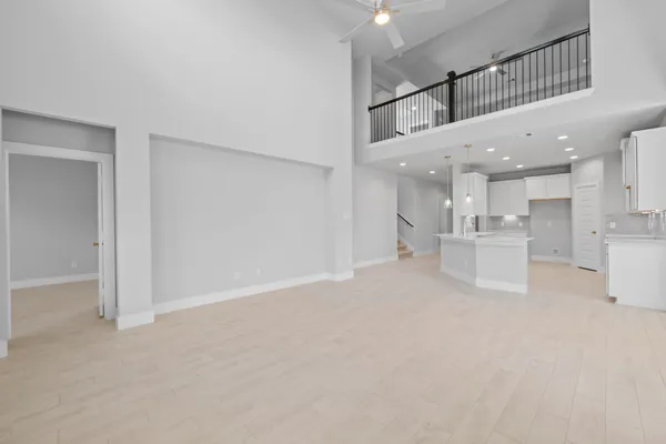 a view of an empty room with a kitchen and chandelier fan