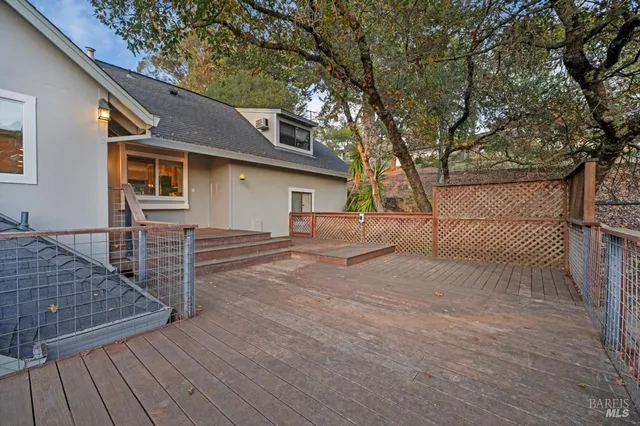 a backyard of a house with wooden floor and fence and a large tree