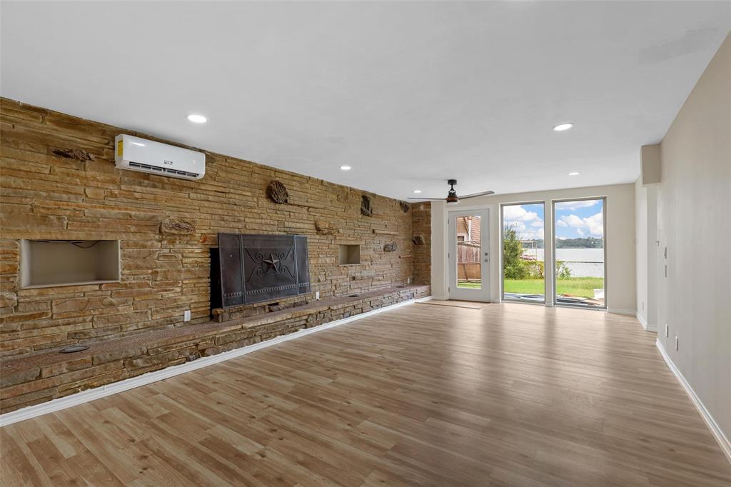 8048 Woodvale Road Fort Worth, TX 76135 - Photo 14 of 27 Unfurnished living room with a wall unit AC, light hardwood / wood-style flooring, a stone fireplace, and ceiling fan