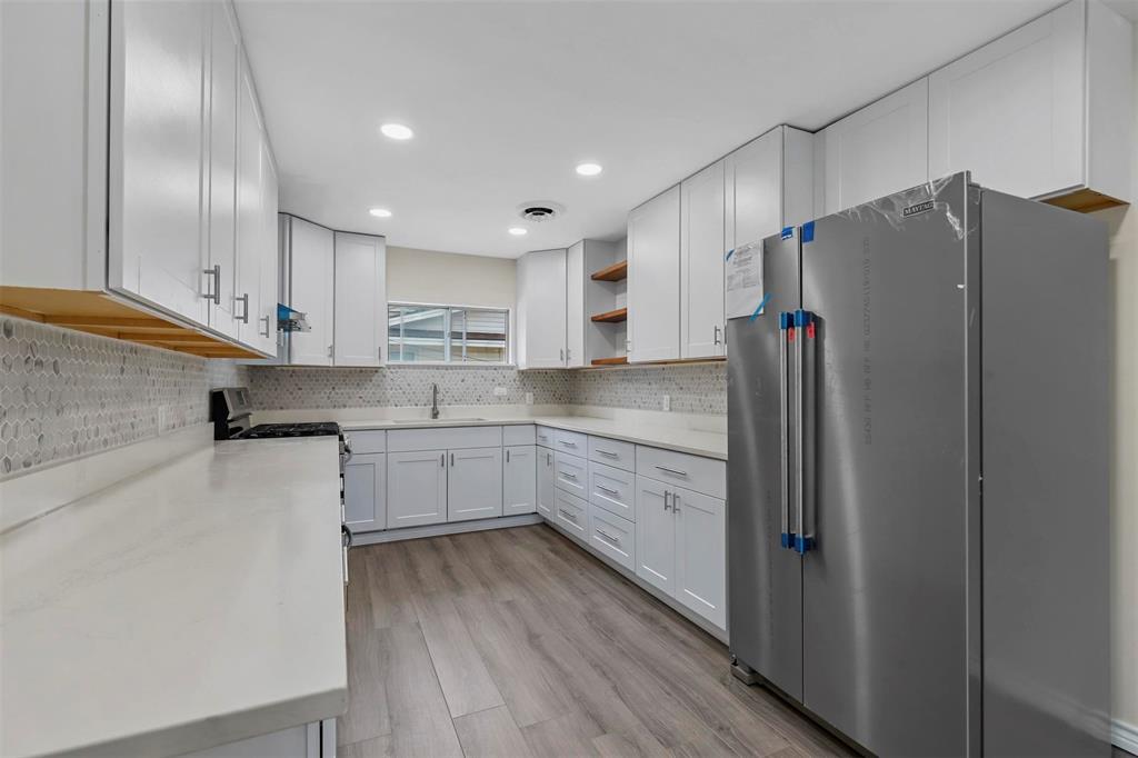 8048 Woodvale Road Fort Worth, TX 76135 - Photo 24 of 27 Kitchen featuring white cabinetry, tasteful backsplash, sink, appliances with stainless steel finishes, and light hardwood / wood-style flooring