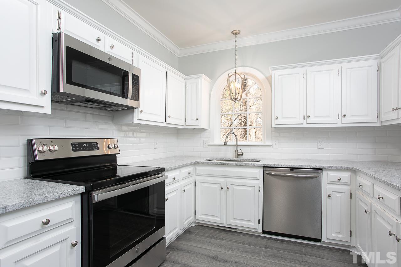 6830 Gloucester Road Raleigh, NC 27612 - Photo 4 of 28 a kitchen with stainless steel appliances granite countertop white cabinets a sink a stove and a microwave