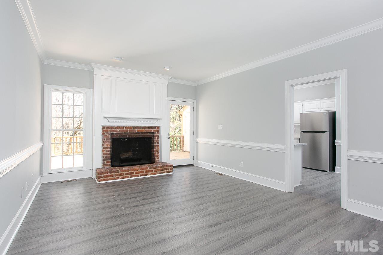6830 Gloucester Road Raleigh, NC 27612 - Photo 7 of 28 an empty room with wooden floor fireplace and windows