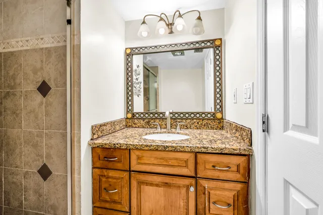 a bathroom with a granite countertop sink a mirror and a shower
