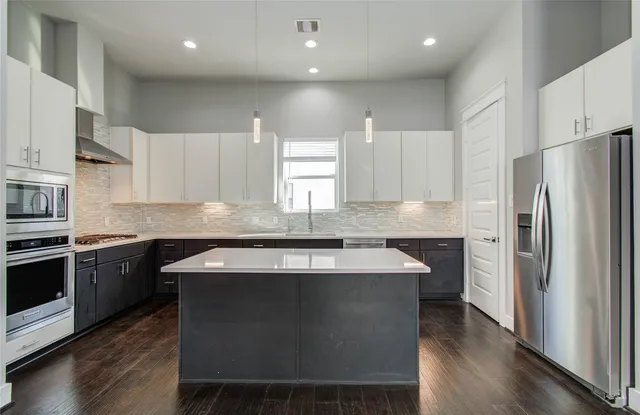 a kitchen with stainless steel appliances granite countertop a stove a refrigerator a sink a stove and white cabinets with wooden floor