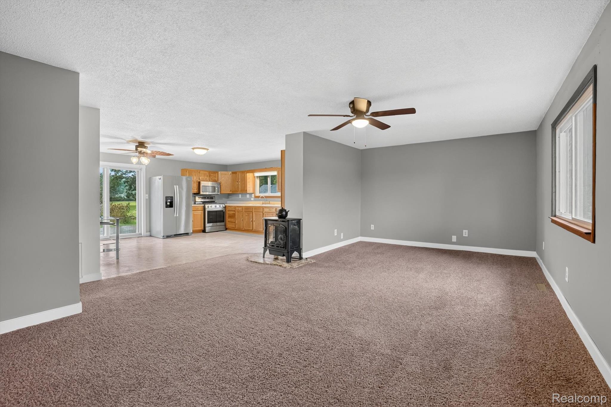 10977 Maple Road Birch Run, MI 48415 - Photo 8 of 49 Spacious room with carpet flooring and a ceiling fan, featuring a wood-burning stove on a stone hearth