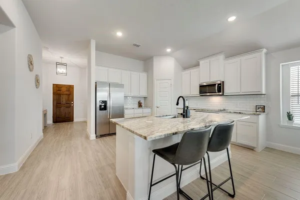 a kitchen with stainless steel appliances granite countertop a table chairs refrigerator and sink