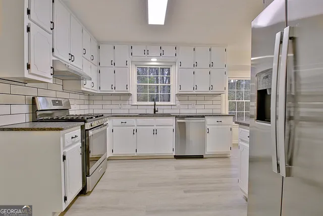 a kitchen with stainless steel appliances granite countertop a stove a sink and white cabinets
