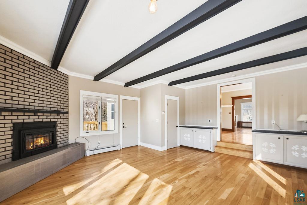 4220 McCulloch Street Duluth, MN 55804 - Photo 5 of 27 Unfurnished living room featuring light wood finished floors, a brick fireplace, a baseboard heating unit, beam ceiling, and ornamental molding