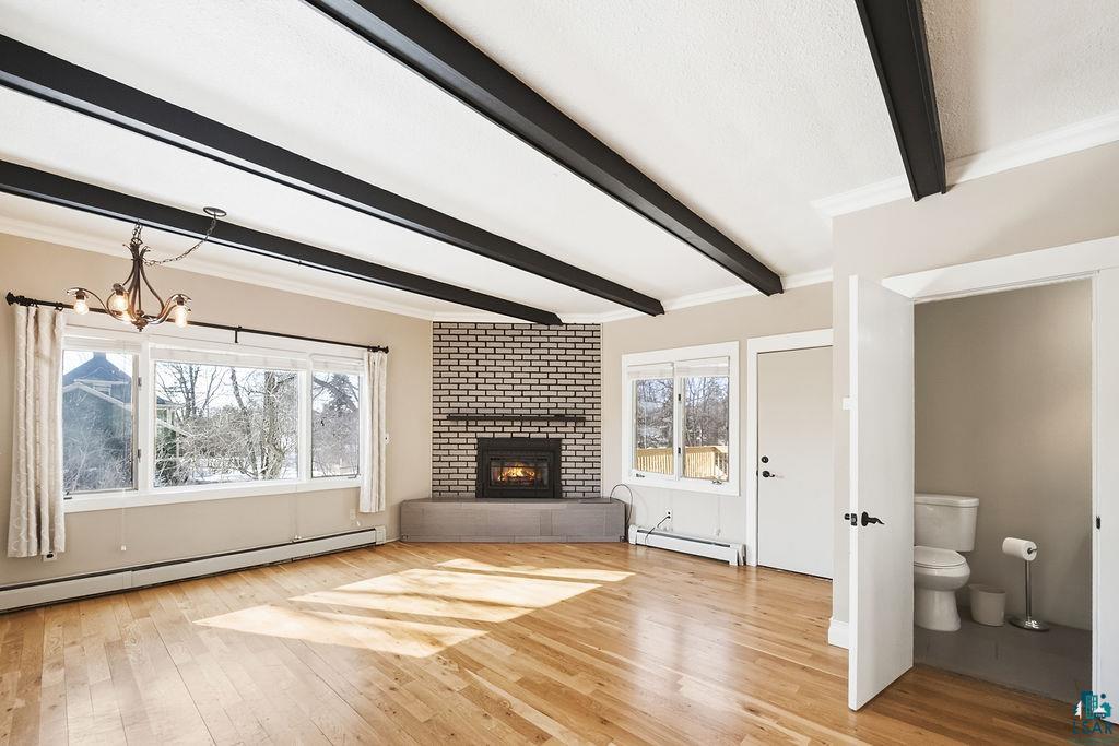 4220 McCulloch Street Duluth, MN 55804 - Photo 6 of 27 Unfurnished living room featuring a baseboard radiator, light wood-type flooring, beam ceiling, a fireplace, and crown molding