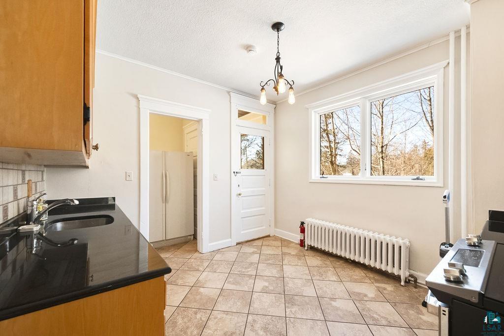 4220 McCulloch Street Duluth, MN 55804 - Photo 8 of 27 Dining room featuring radiator, a textured ceiling, hanging lights, light tile patterned floors, and crown molding