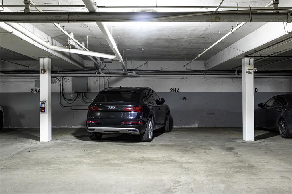 3922 Gilbert Avenue, Unit 214 Dallas, TX 75219 - Photo 24 of 27 Designated parking space within a concrete garage structure, featuring exposed overhead piping, concrete columns, and wall-mounted electrical conduits