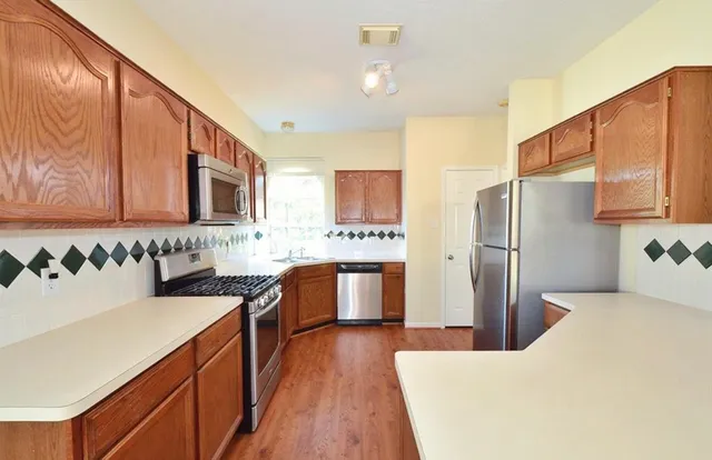 a kitchen with stainless steel appliances granite countertop a refrigerator a stove top oven a sink dishwasher and wooden cabinets with wooden floor