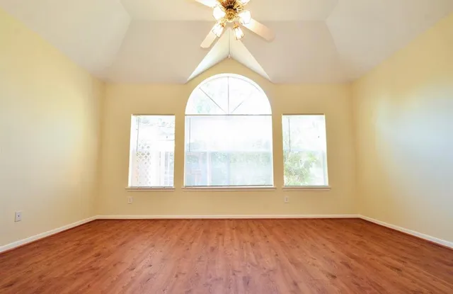 an view of an empty room with wooden floor and a window