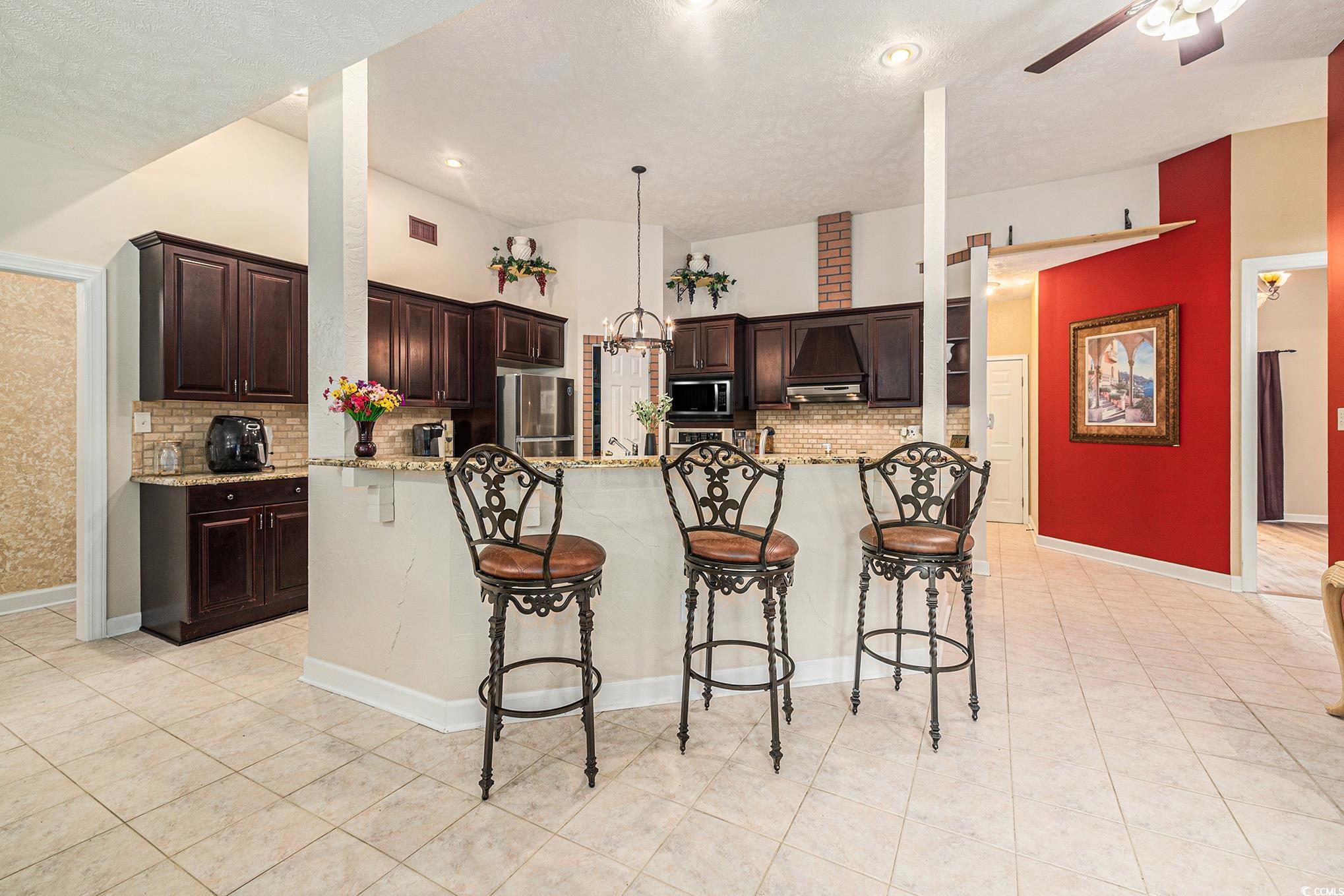 2425 Hunters Trail Myrtle Beach, SC 29588 - Photo 14 of 40 Kitchen featuring tasteful backsplash, a breakfast bar area, a ceiling fan, dark brown cabinetry, and a textured ceiling