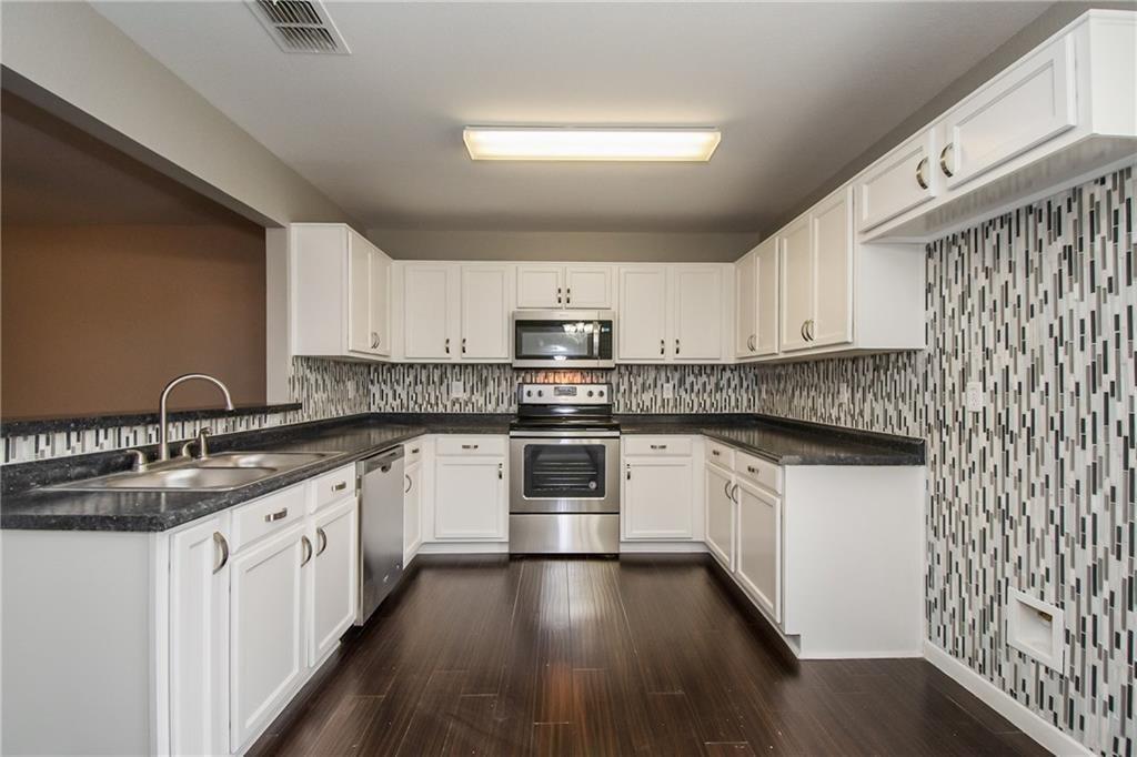 926 Walnut Street Burleson, TX 76028 - Photo 14 of 17 Kitchen featuring stainless steel appliances, white cabinets, dark wood-type flooring, and backsplash