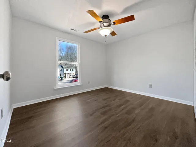 an empty room with wooden floor fan and windows