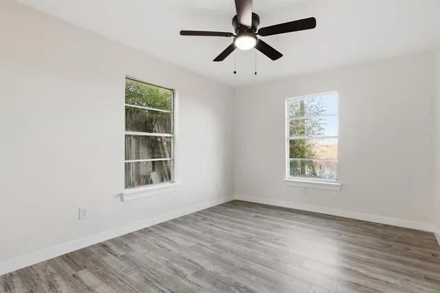 an empty room with wooden floor ceiling fan and windows