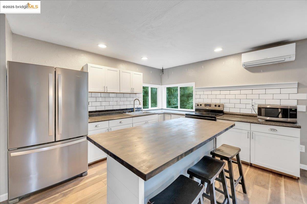21980 Montgomery Road Sonora, CA 95370 - Photo 13 of 52 Kitchen with appliances with stainless steel finishes, a breakfast bar area, white cabinets, a wall unit AC, and light wood-type flooring