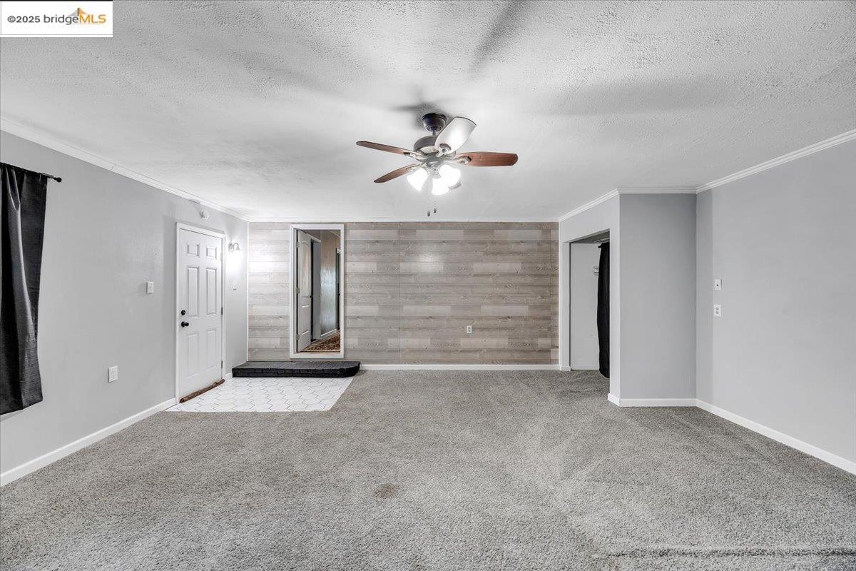 21980 Montgomery Road Sonora, CA 95370 - Photo 24 of 52 Carpeted empty room featuring wooden walls, an accent wall, a textured ceiling, ceiling fan, and crown molding