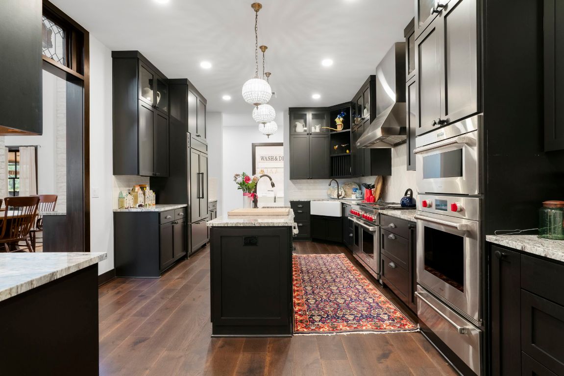 4073 Bell Springs Road Dripping Springs, TX 78620 - Photo 23 of 38 a kitchen with stainless steel appliances kitchen island granite countertop a stove a sink dishwasher and a refrigerator with wooden floor
