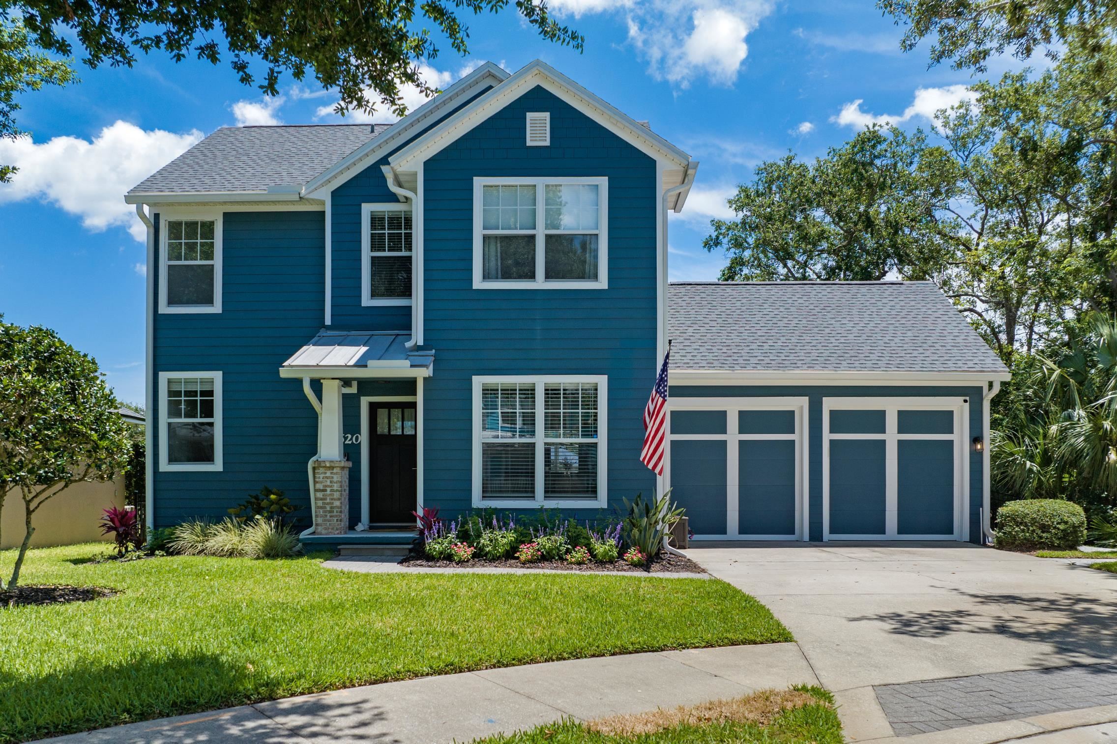 a view of a brick house with a yard plants and a large tree