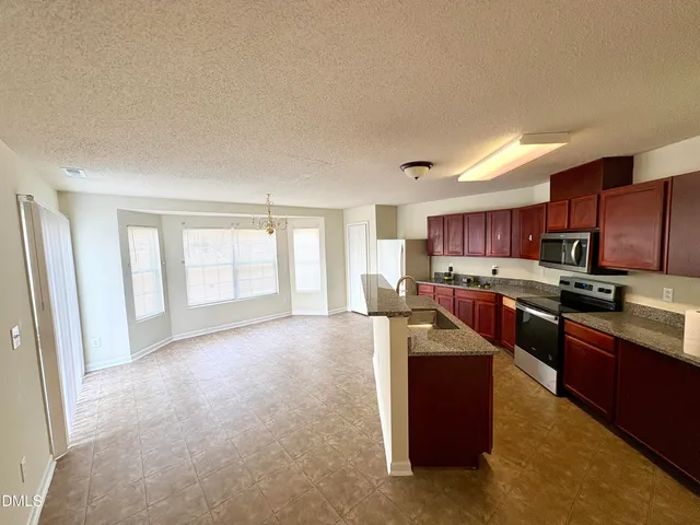 a large kitchen with stainless steel appliances granite countertop a refrigerator a sink a stove a microwave a counter space and cabinets