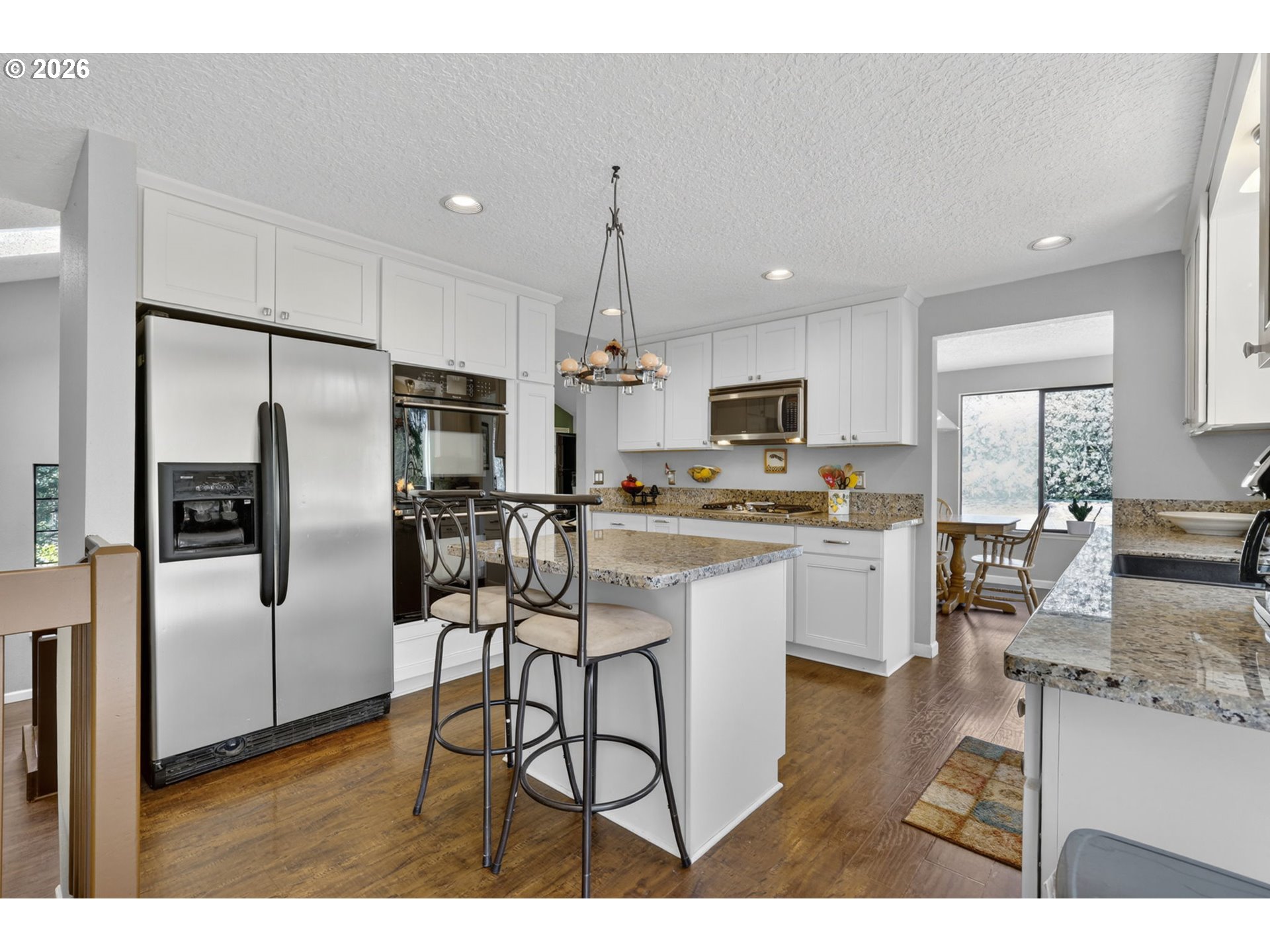 21155 Southeast Foster Road Damascus, OR 97089 - Photo 17 of 48 a kitchen with stainless steel appliances kitchen island granite countertop a refrigerator a stove a sink a dining table and chairs with wooden floor