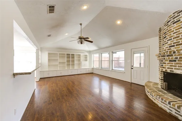 an empty room with wooden floor chandelier fan and windows