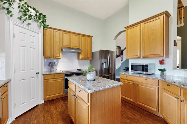 a kitchen with stainless steel appliances granite countertop a stove a sink dishwasher and a refrigerator with wooden floor