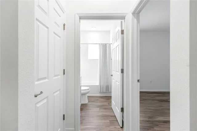 a view of a hallway with wooden floor and a bathroom