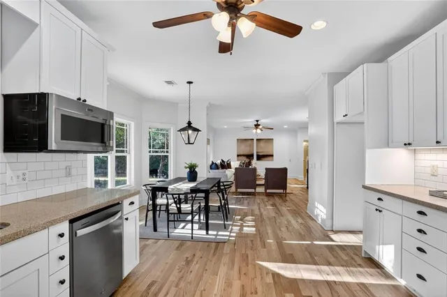 a open kitchen with stainless steel appliances kitchen island granite countertop a stove top oven a sink a dining table and chairs with wooden floor