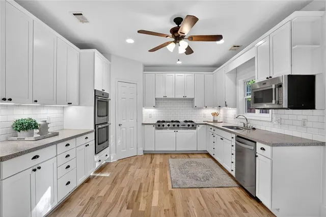 a kitchen with granite countertop a refrigerator a sink dishwasher a stove and white cabinets with wooden floor