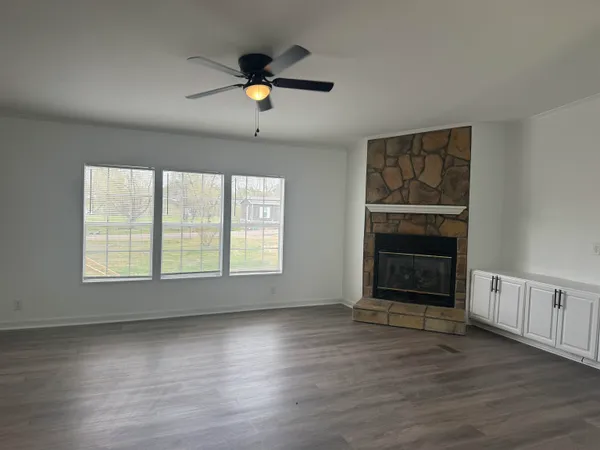 an empty room with wooden floor fan and windows