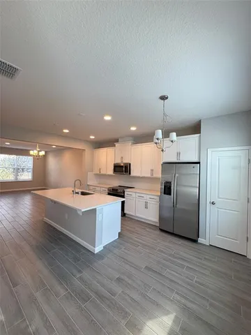 a kitchen with stainless steel appliances kitchen island granite countertop a refrigerator a oven a island and couches with wooden floor