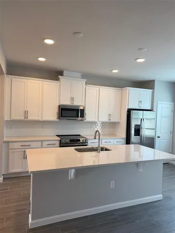 a view of a kitchen with kitchen island a sink wooden floor and stainless steel appliances