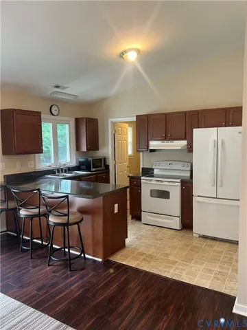 a kitchen with granite countertop a stove top oven a sink dishwasher a refrigerator and a dining table with wooden floor