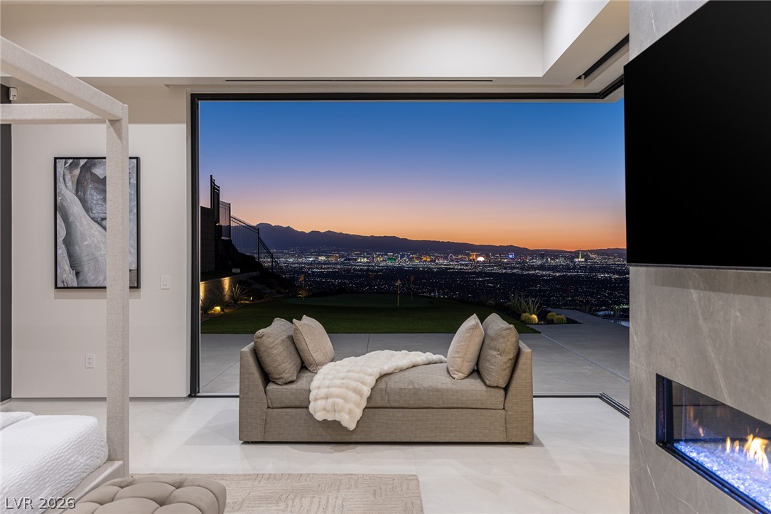 563 Grand Rim Drive Henderson, NV 89012 - Photo 47 of 70 City lights stretch endlessly from this primary bedroom, featuring a sleek fireplace and a view of the vibrant skyline.